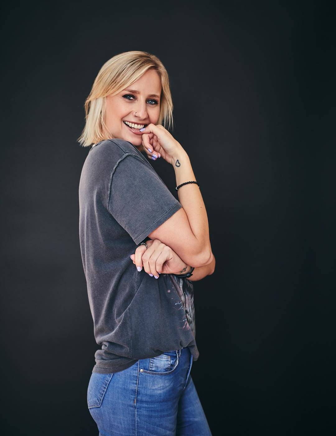 Cat weariing a grey shirt and blue jeans, smiling at the camera.