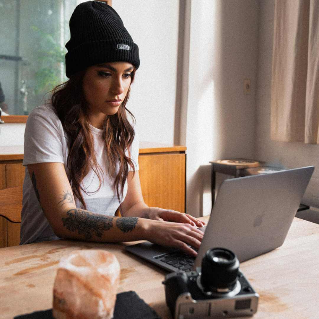 A girl wearing a white t-shirt and black hat working on a laptop