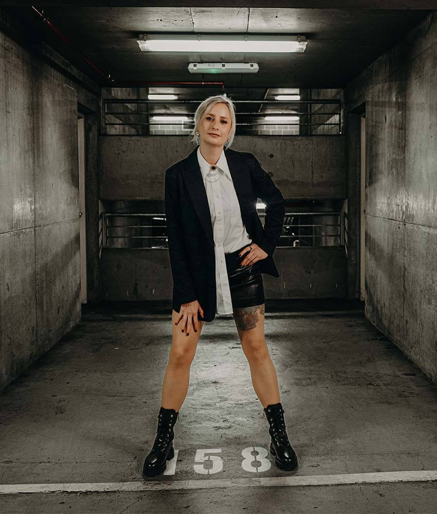 Cat Dunn, an OBM mentor, posing in an underground car park in a suit and leather skirt.