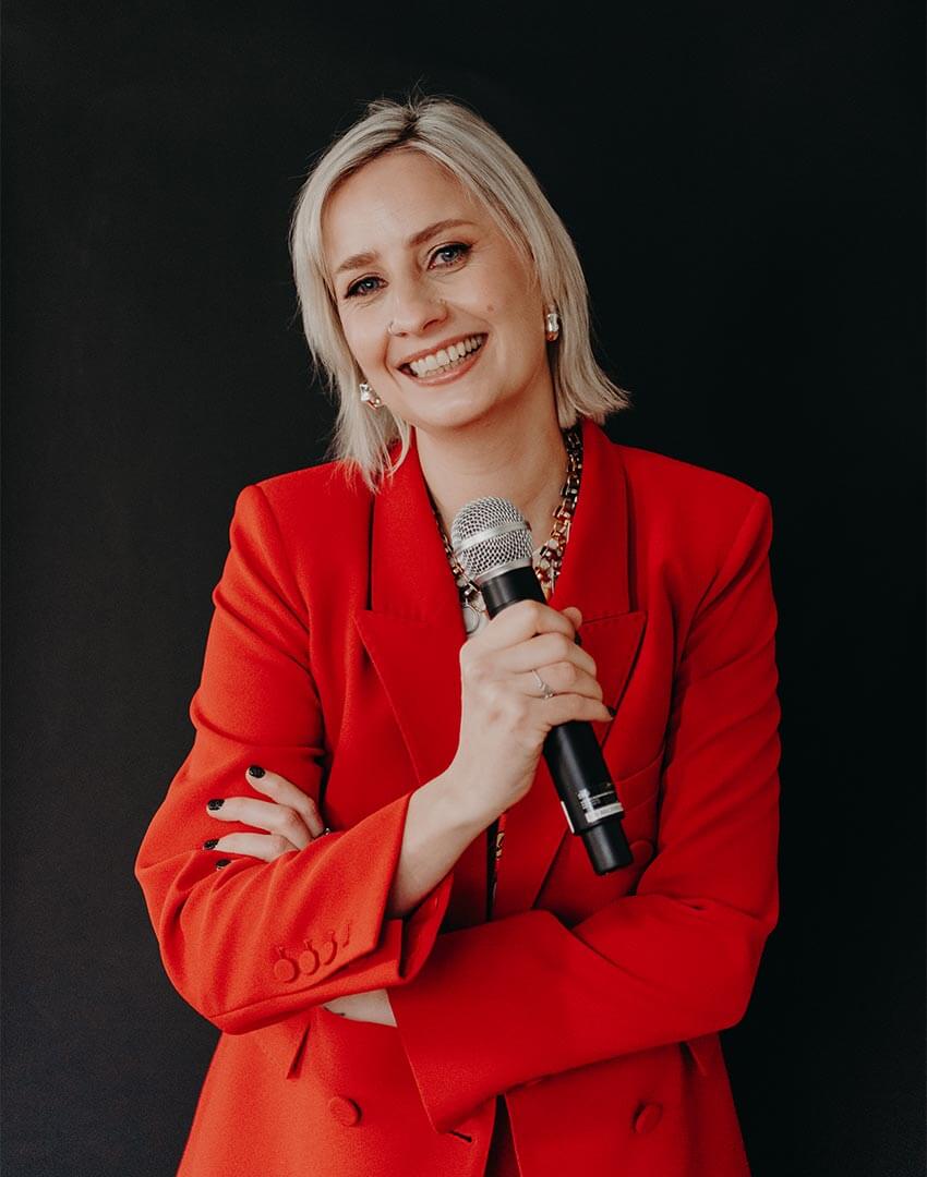 Cat Dunn, speaker and award-winning online business manager, in a red suit holding a microphone.