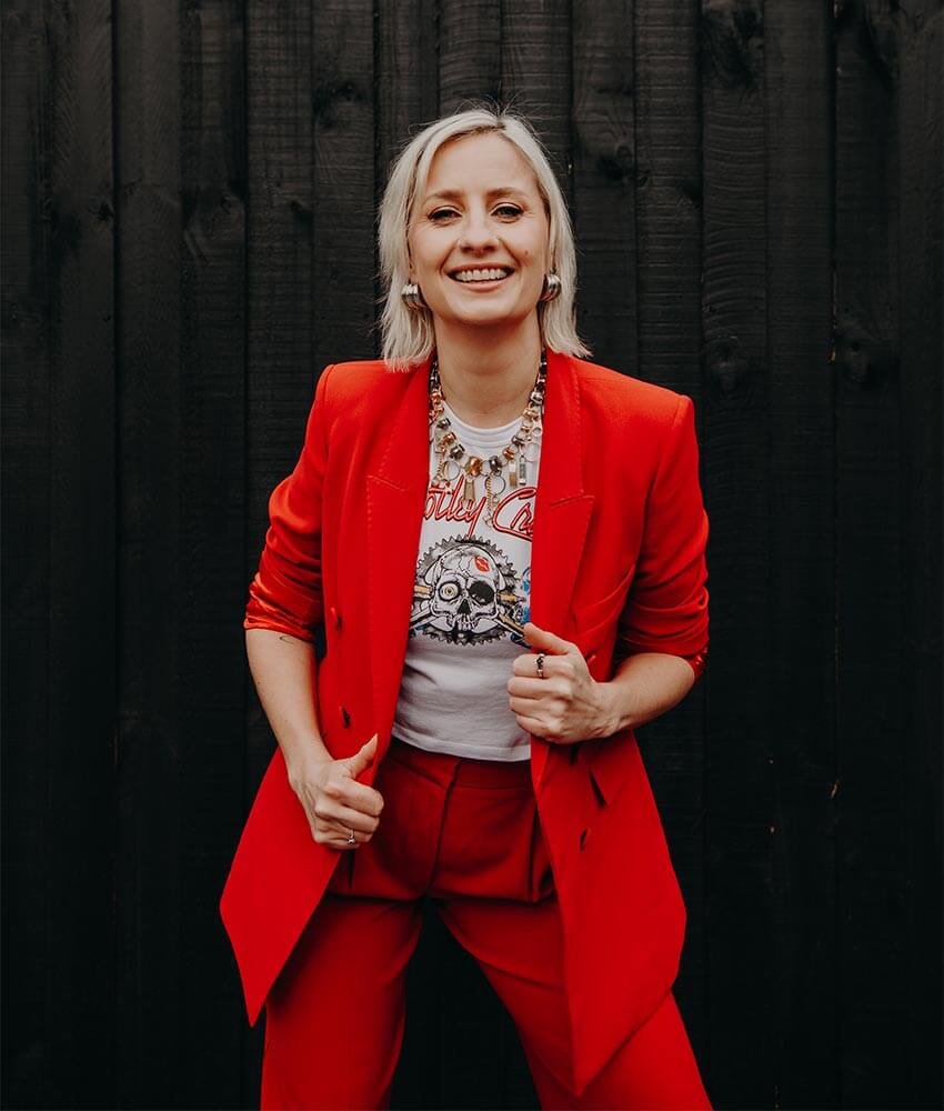 Cat Dunn, an OBM based in Melbourne, wearing a red suit with a Motley Crue tshirt.