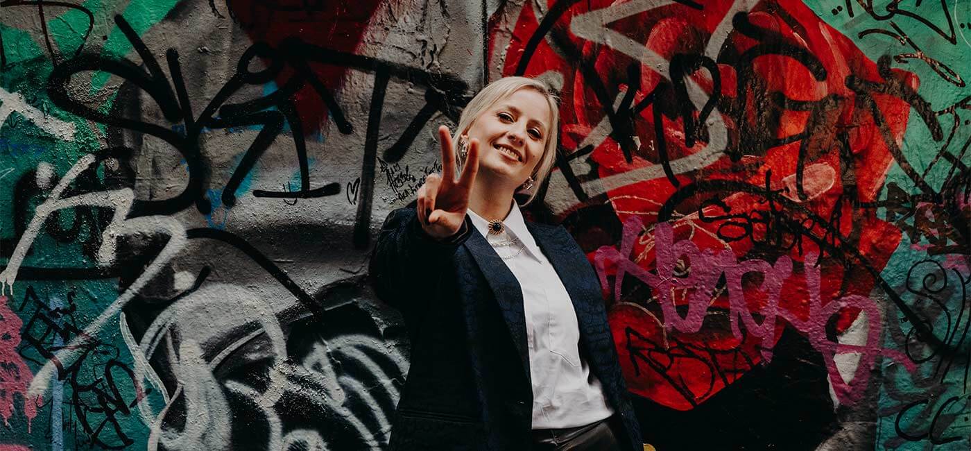 An online business manager holding up the peace sign in front of a colourful graffiti wall.