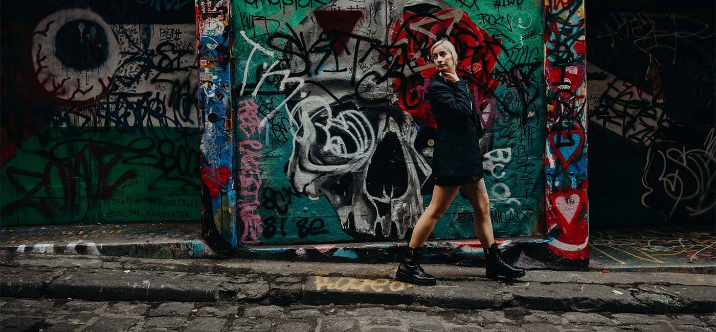 Cat Dunn walking in Melbourne in front of a colourful wall of graffiti, looking behind her.