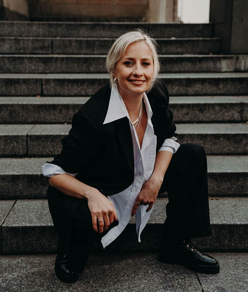 Cat Dunn crouching down on brick stairs in Melbourne in a suit.