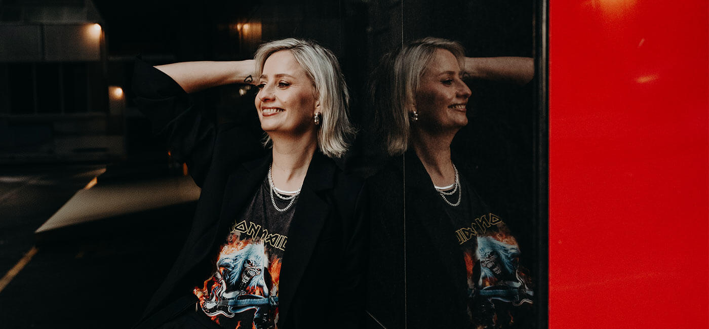 Cat Dunn, mentor to VAs, leaning against a reflective wall wearing an iron maiden shirt.